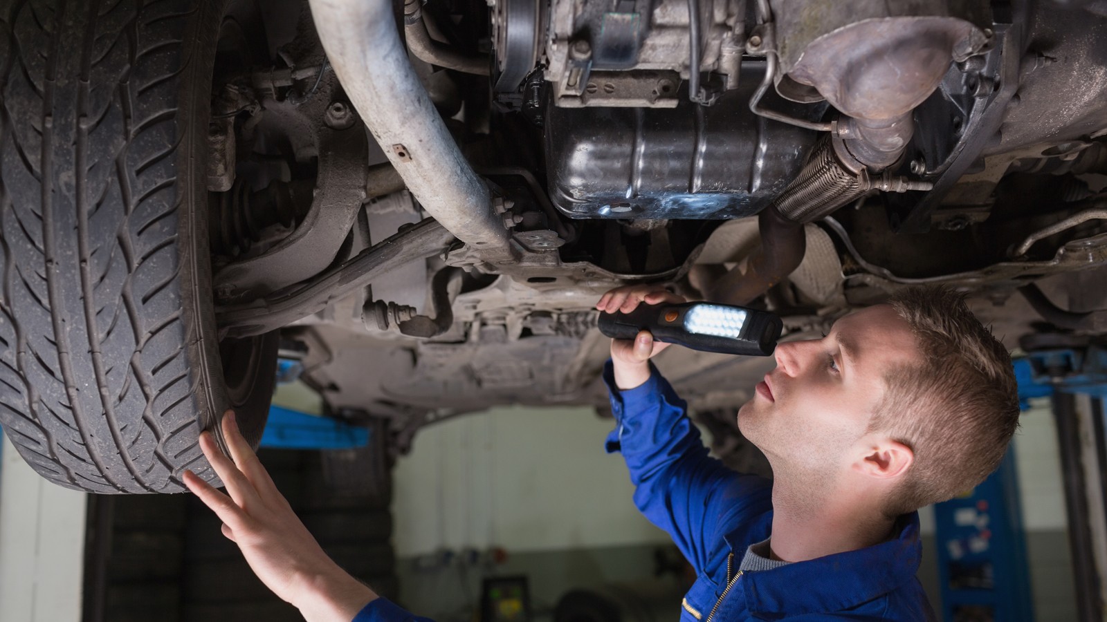 Male mechanic examining car using flashlight