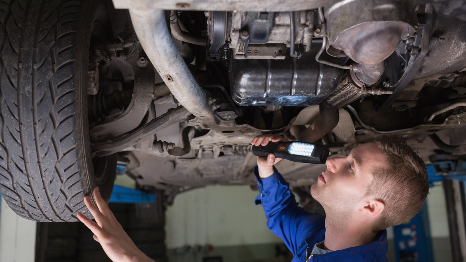 Male mechanic examining car using flashlight