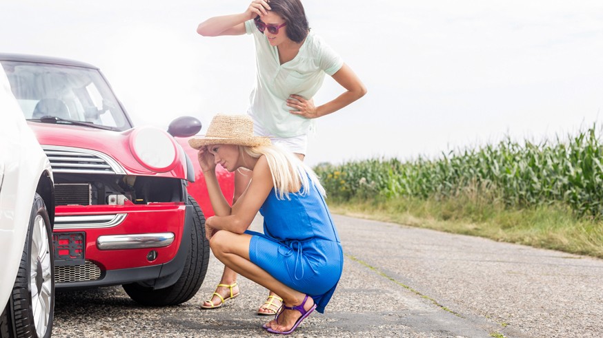 Tensed women looking at damaged cars on road against clear sky