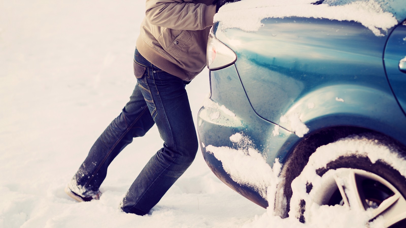 closeup of man pushing car stuck in snow