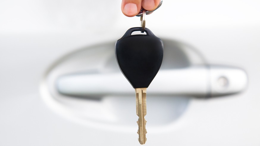 hand holding car key before door of car