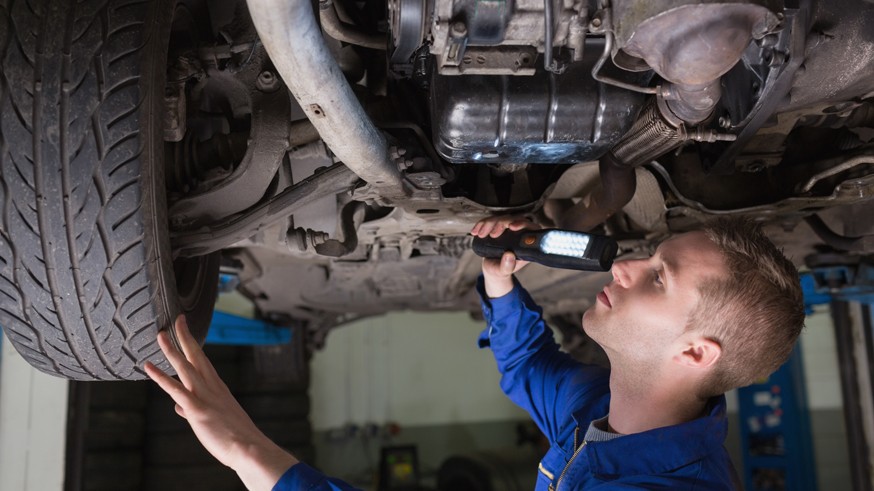Male mechanic examining car using flashlight