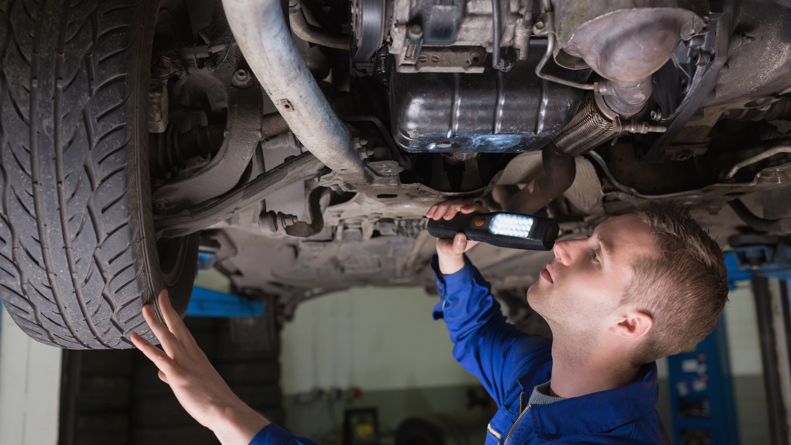 Male mechanic examining car using flashlight