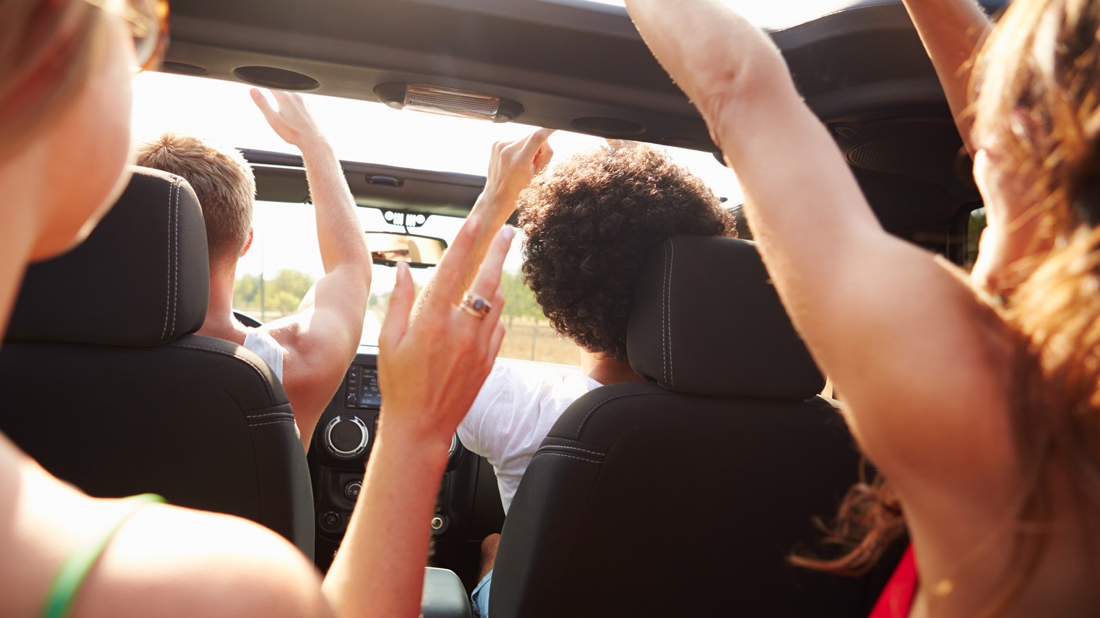 Group Of Young Friends Dancing In Back Of Open Top Car