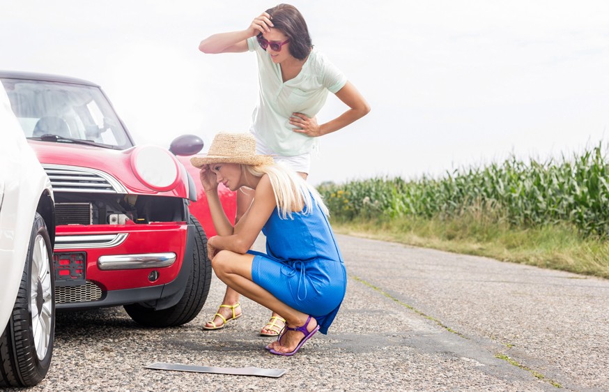 Tensed women looking at damaged cars on road against clear sky