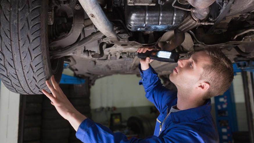 Male mechanic examining car using flashlight