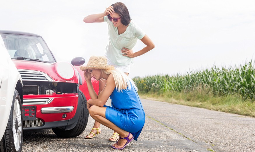 Tensed women looking at damaged cars on road against clear sky
