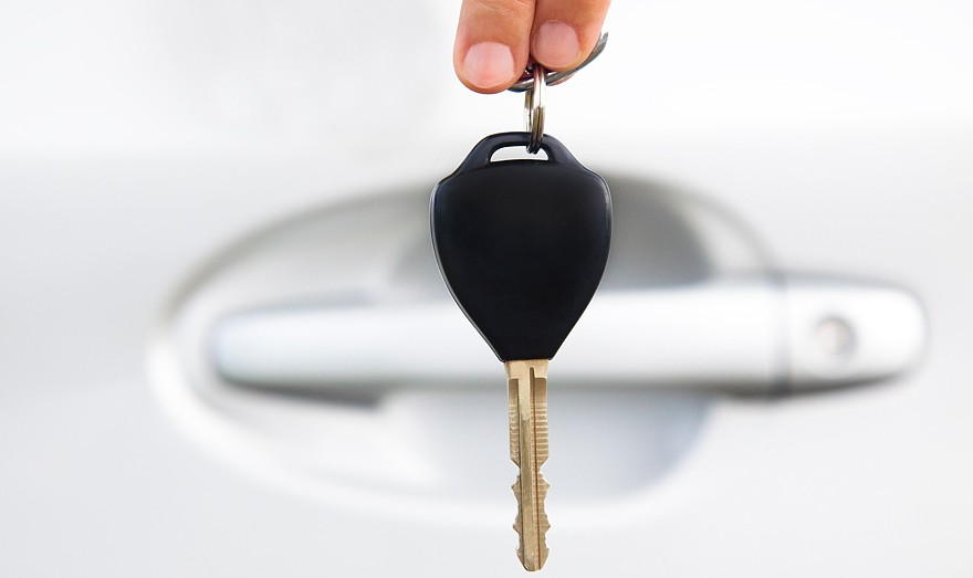 hand holding car key before door of car