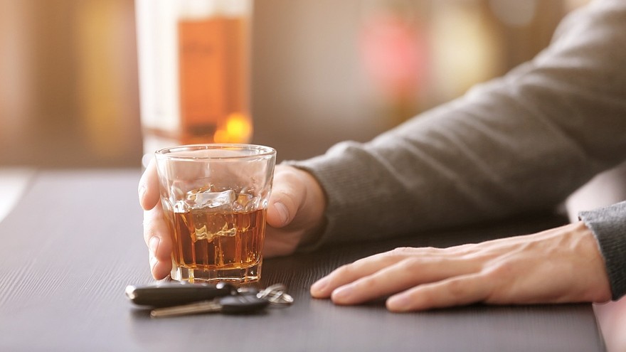 Man sitting in bar with car key and glass of alcoholic beverage, closeup. Don't drink and drive concept