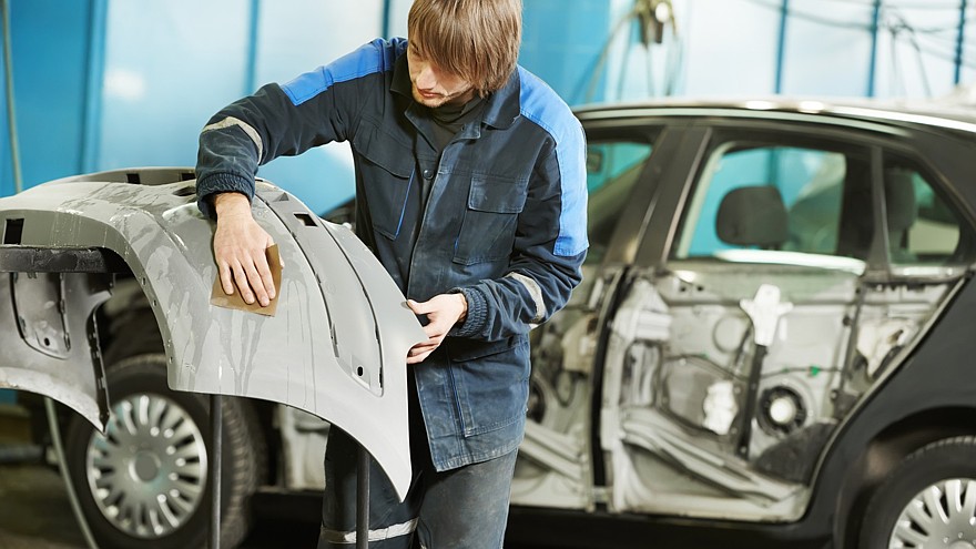 repairman sanding plastic car bumper