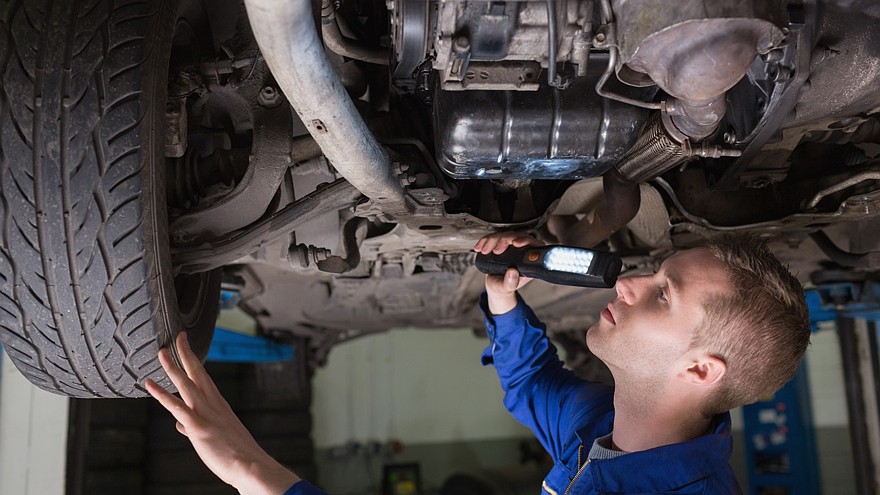 Male mechanic examining car using flashlight